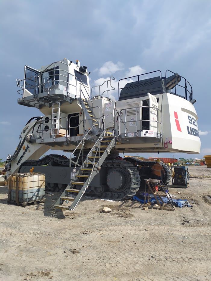 A massive Liebherr excavator at a construction site under a cloudy sky in Kalimantan Selatan, Indonesia.