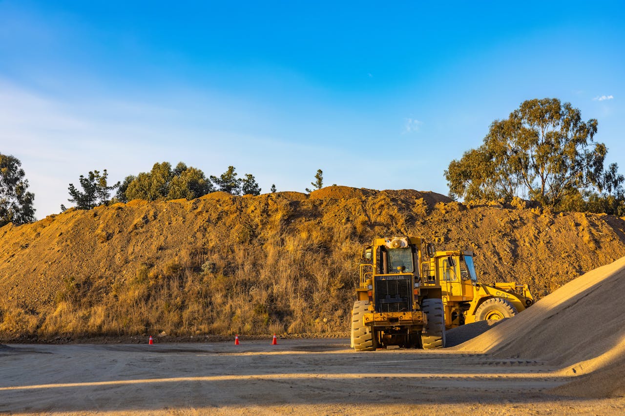 who-we-are Yellow construction machinery working on a dirt pile at a rural site with a clear blue sky backdrop.